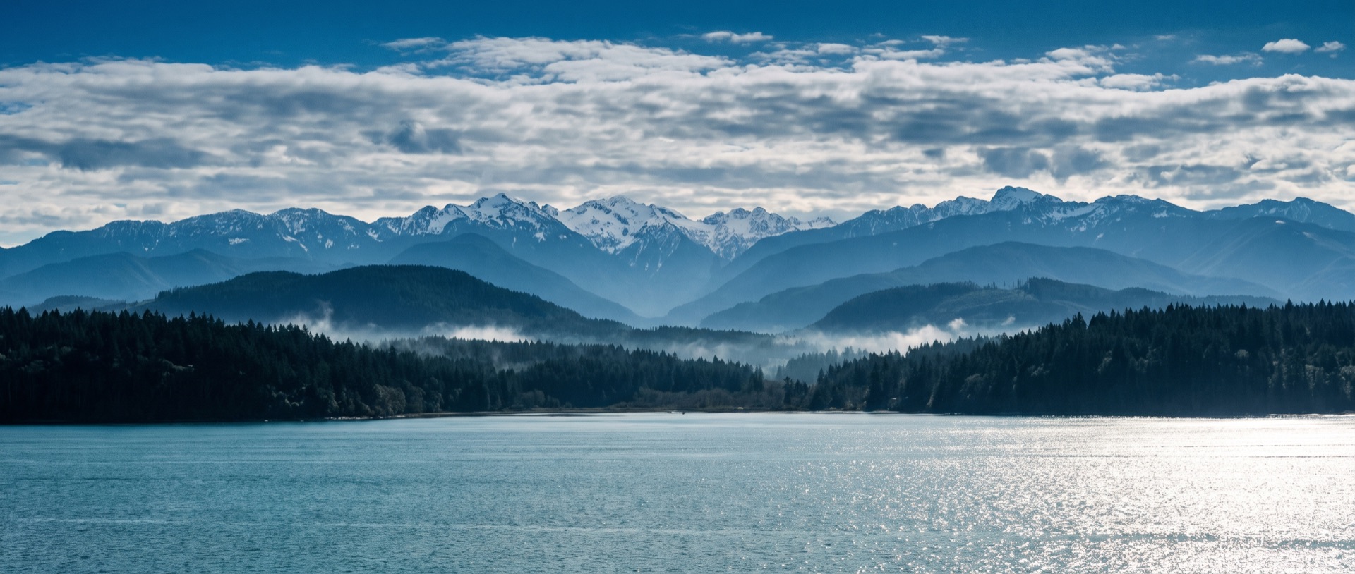 Puget Sound looking west to the Olympic Mountains: layered ranges fading into blue haze, snow on the high peaks.